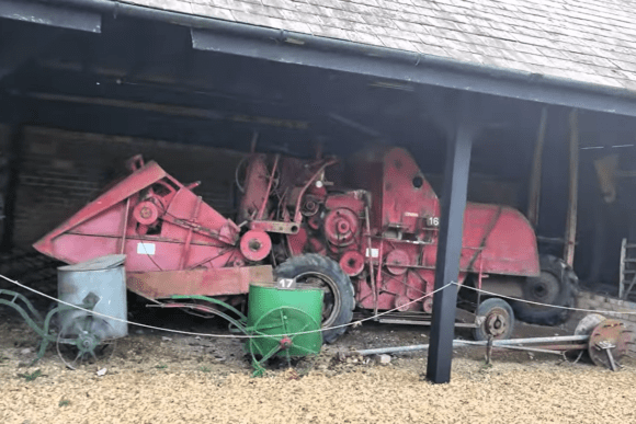 Vintage red agricultural machinery displayed under a farm shed at Denny Abbey & Farmland Museum.