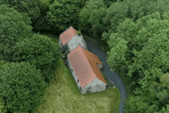 Aerial view of Derwentcote Steel Furnace buildings with red-tiled roofs, surrounded by dense woodland and a winding path.