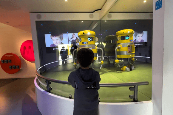 Child interacting with a robotic exhibit at Eureka! The National Children’s Museum, watching two animated yellow robots inside an immersive technology and learning display.