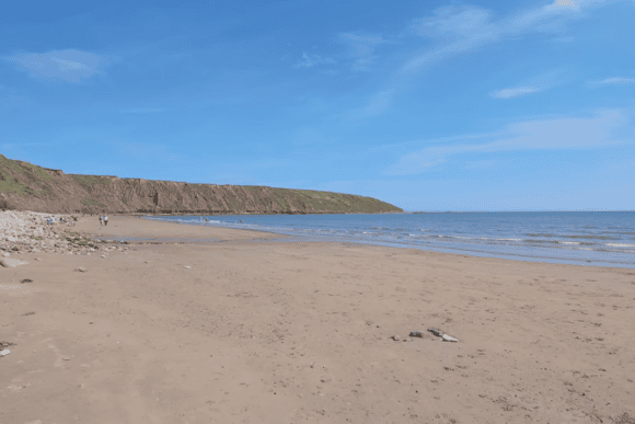 Wide view of Filey Beach in North Yorkshire with golden sand, gentle waves, dramatic cliffs, and clear blue skies along the scenic Yorkshire coastline.