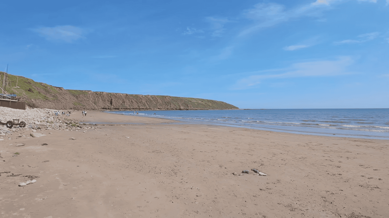 Wide view of Filey Beach in North Yorkshire with golden sand, gentle waves, dramatic cliffs, and clear blue skies along the scenic Yorkshire coastline.