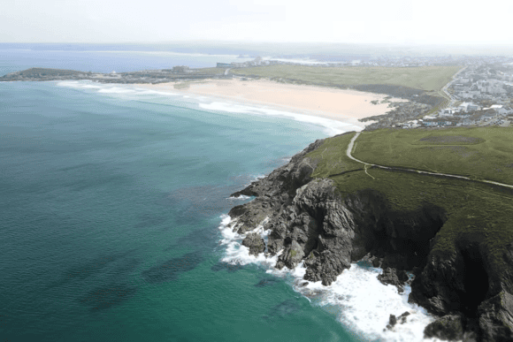 Aerial panorama of Fistral Beach in Newquay, Cornwall, featuring turquoise Atlantic waters, golden sandy shoreline, rugged cliffs, and the surrounding coastline.