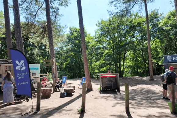 National Trust visitor area at Formby Beach with tall pine trees, information kiosk, café, and woodland entrance leading to the famous sand dunes and coastline in Merseyside.