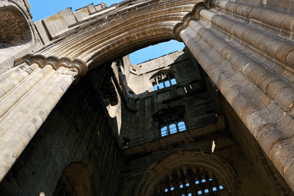 Upward view of Fountains Abbey stone arches and ribbed columns framing the open sky above.