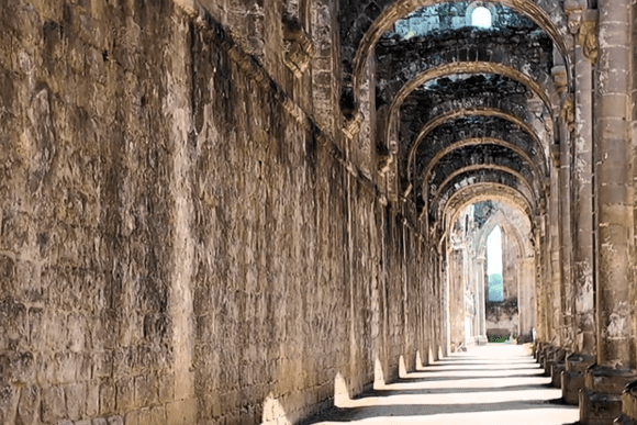Long stone arcade at Fountains Abbey with repeating arches and sunlight illuminating the floor.
