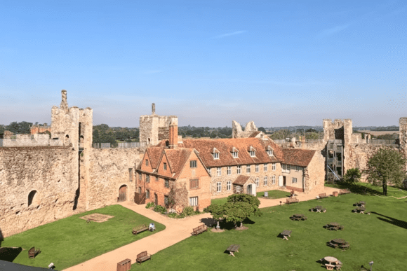 View inside Framlingham Castle showing the inner courtyard, historic brick buildings, and surrounding stone curtain walls under a clear sky.