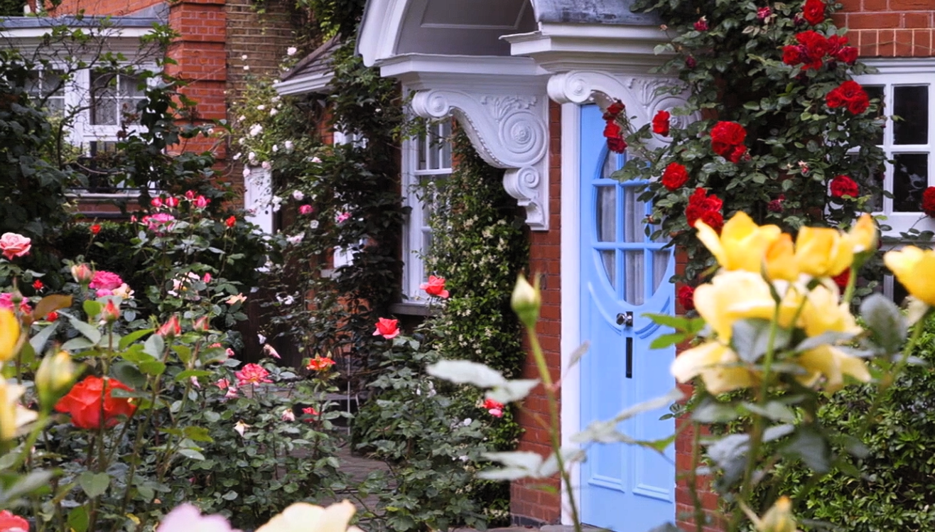 Rose-filled garden framing a pale blue front door at the Freud Museum, with red brick walls and climbing flowers.