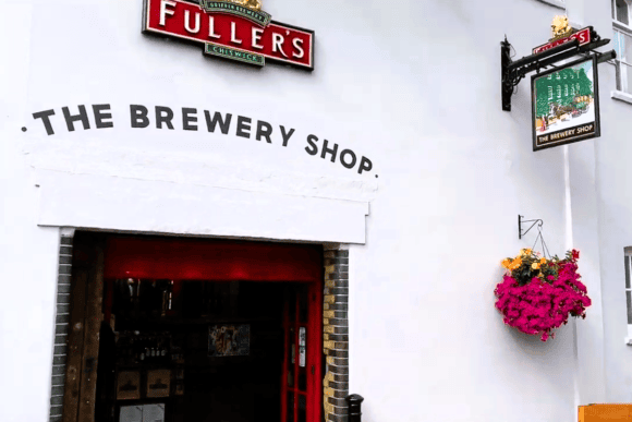 Fuller's Griffin Brewery Shop entrance in Chiswick, London, featuring the iconic Fuller's sign, brewery shop entrance, and hanging flower basket.