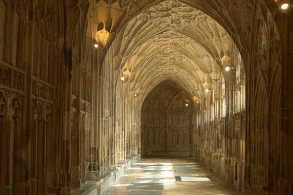 Fan-vaulted cloister corridor inside Gloucester Cathedral with carved stone arches and soft lighting along the walkway.