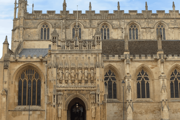 Detailed view of Gloucester Cathedral’s ornate Gothic entrance with carved stone statues above the arched doorway and tall traceried windows.