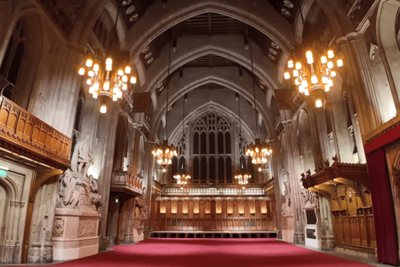 Interior of Guildhall London showing a grand Gothic hall with vaulted ceilings, chandeliers, carved stone statues, and red carpet.