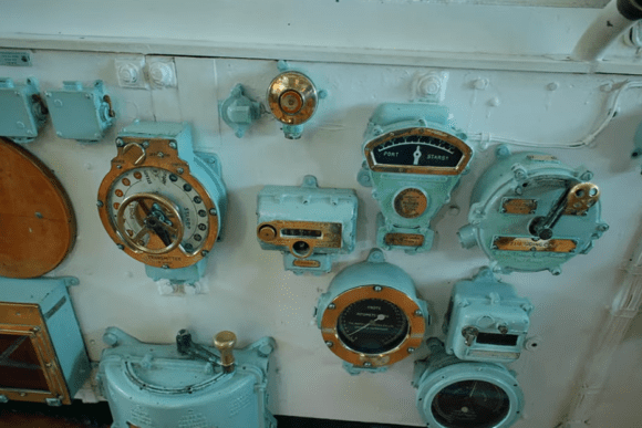 Vintage naval control instruments and gauges mounted on a wall inside HMS Belfast.