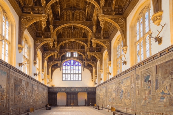 Interior of Hampton Court Palace’s Great Hall with a hammerbeam wooden ceiling, stained glass windows, and large historic tapestries.