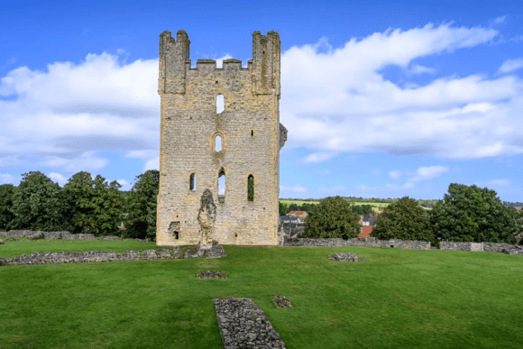 Ruined medieval tower of Helmsley Castle standing on a grassy field under a blue sky.