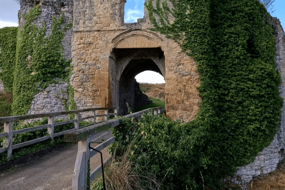 Stone entrance arch of Helmsley Castle with a wooden bridge and ivy-covered walls.