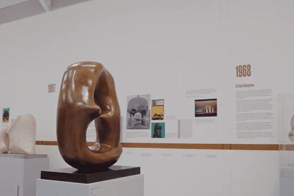 Abstract bronze sculpture with a hollowed organic form displayed at the Henry Moore Institute in Leeds, surrounded by modern artworks and exhibition panels exploring twentieth-century sculpture.