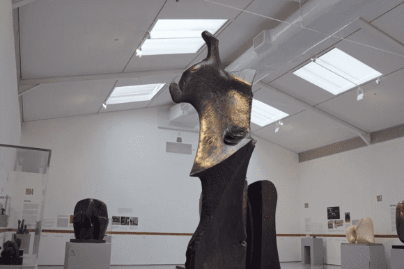 Tall abstract bronze sculpture displayed in a bright gallery at the Henry Moore Institute in Leeds, surrounded by modern sculptures and exhibition displays showcasing twentieth-century British sculpture.