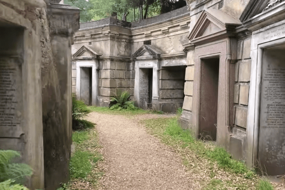 Row of stone mausoleums lining a pathway inside Highgate Cemetery in London.