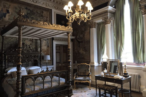 Elegant historic bedroom with four-poster bed, chandelier, and classical décor inside Holkham Hall.