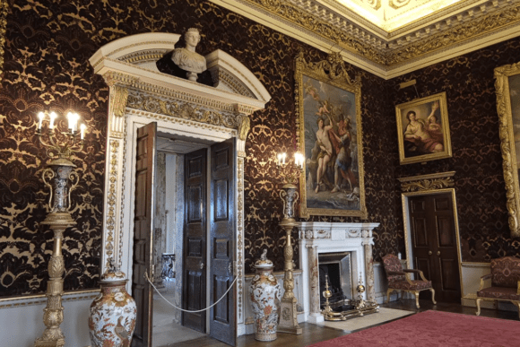 Lavishly decorated room at Holkham Hall with paintings, fireplace, and ornate wallpaper.