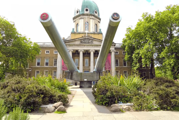 Naval guns outside the Imperial War Museum building with a domed roof in London.