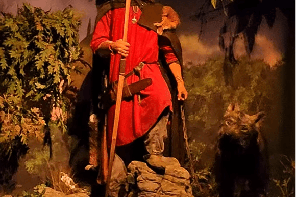 Viking warrior exhibit at JORVIK Viking Centre in York featuring a life-sized Norse figure in traditional clothing holding a spear, accompanied by a hunting dog in a woodland setting.