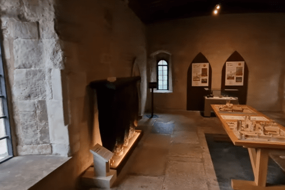 Interior of Jewel Tower museum showing medieval stone room with display panels and a model exhibit.