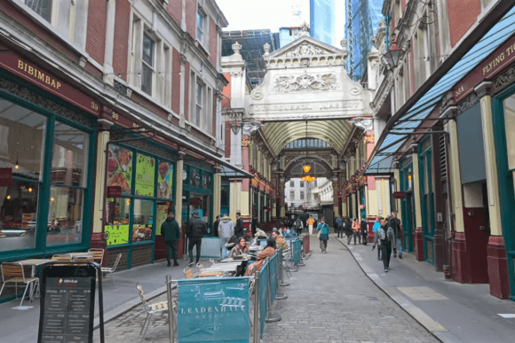 Leadenhall Market street view with shops, pedestrians, and outdoor seating beneath an ornate covered arcade.