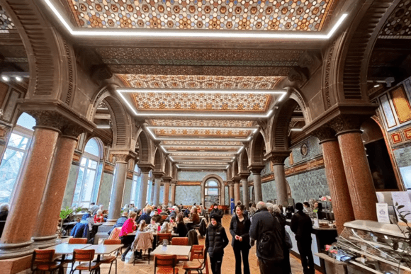Historic café interior at Leeds Art Gallery featuring ornate Victorian architecture, decorative ceilings, grand arches, marble columns, and visitors dining beneath richly detailed heritage interiors.