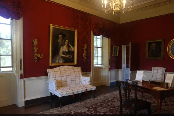 Elegant red-walled interior room at Marble Hill House with paintings, chairs, and a central table.