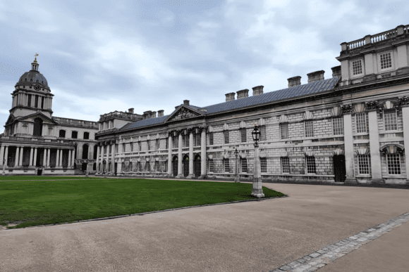 Side view of the Old Royal Naval College in Greenwich with colonnades, dome, and courtyard lawn.