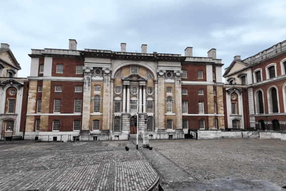 Front view of a classical red-brick building at the Old Royal Naval College with columns and central arch.