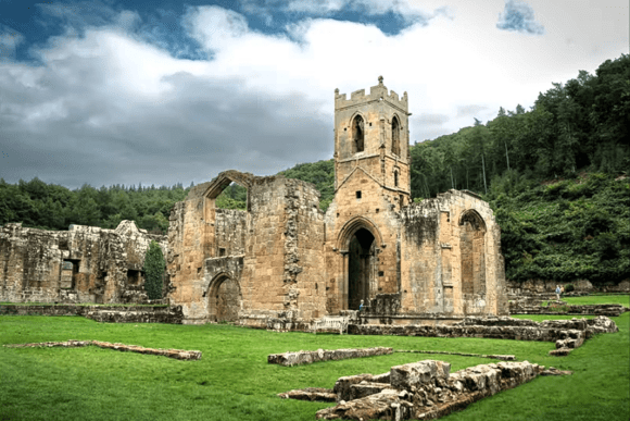 Ruins of Mount Grace Priory church with tower and arches set in green countryside.