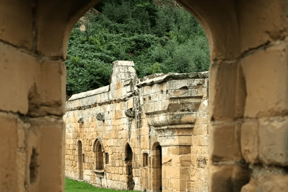 View through a stone archway framing Mount Grace Priory ruins with arched windows and grassy courtyard.