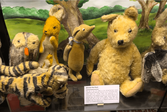 Vintage Winnie-the-Pooh and Hundred Acre Wood character toys displayed at the Museum of Brands in London, featuring classic plush figures including Pooh Bear, Tigger, Owl, Rabbit, and Piglet in a nostalgic exhibition case.