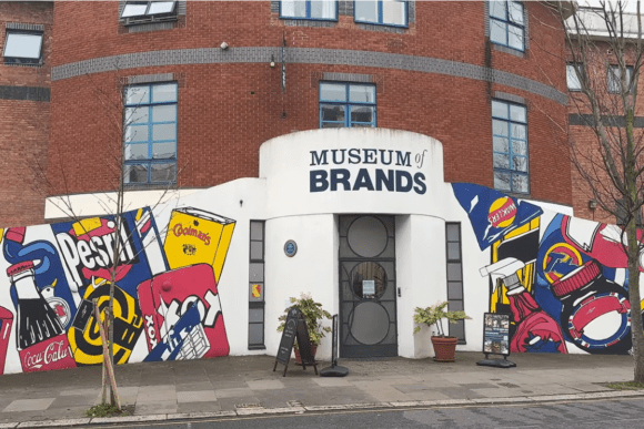 Exterior entrance of the Museum of Brands in London, featuring a colourful pop-art mural with iconic consumer product imagery surrounding the museum’s main doorway.