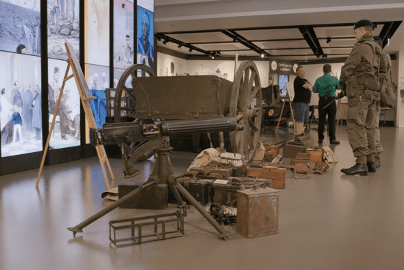 Historic military equipment display at the National Army Museum in London, featuring a machine gun, ammunition boxes, transport cart, and a soldier mannequin illustrating British Army wartime history.