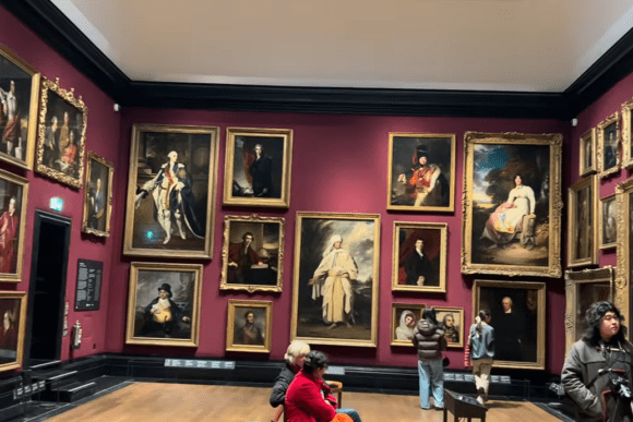 Visitors viewing large framed portraits on deep red walls inside the National Portrait Gallery.