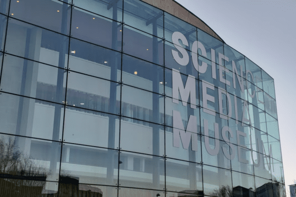Glass façade of the National Science and Media Museum in Bradford, featuring large museum branding across a modern architectural exterior dedicated to photography, film, television, and digital media.