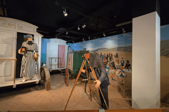 Vintage photography exhibit at the National Science and Media Museum featuring a historic camera setup, seaside scene recreation, beach huts, and interactive displays exploring the early history of photography.