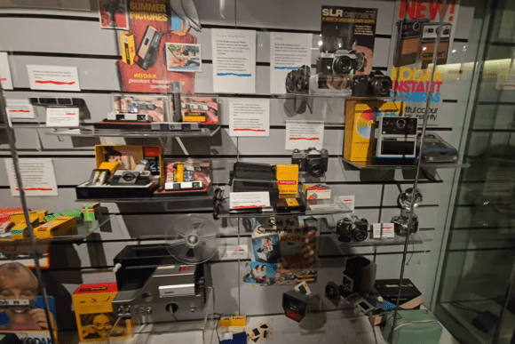 Vintage camera collection displayed at the National Science and Media Museum, featuring Kodak cameras, instant cameras, film equipment, photography accessories, and historic advertising materials documenting the evolution of consumer photography.