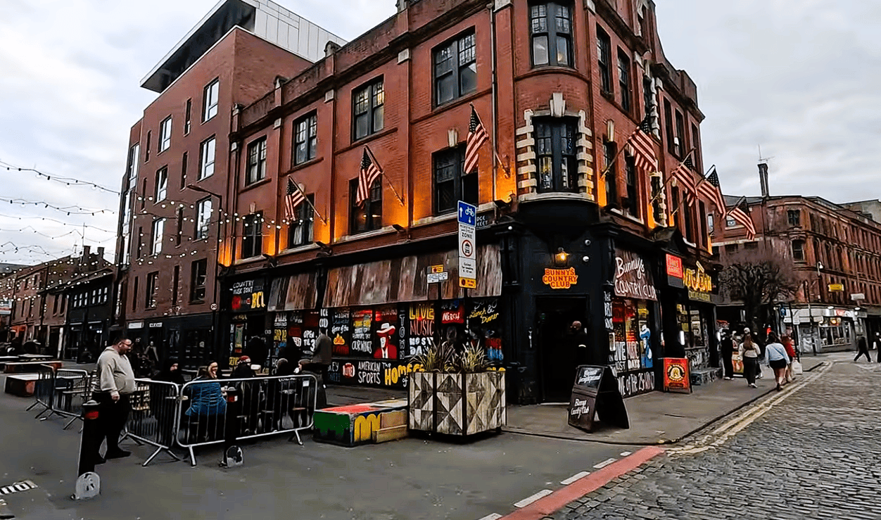 Street scene in Manchester’s Northern Quarter featuring Bunny’s Country Club, colourful artwork, outdoor seating and historic red-brick buildings.