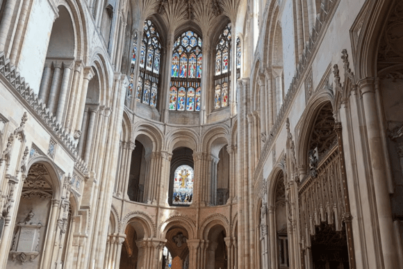 Interior of Norwich Cathedral apse with tall stone arches and colorful stained-glass windows.