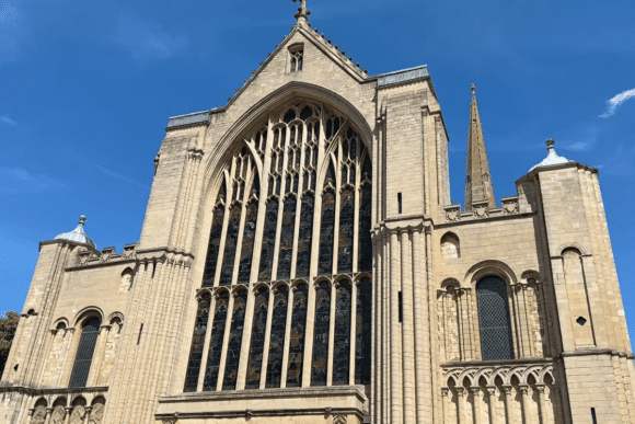 Front façade of Norwich Cathedral featuring a large stained-glass window and Gothic stone architecture.