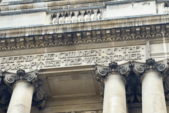Stone inscription on the Old Bailey façade reading “Defend the children of the poor & punish the wrongdoer,” above classical columns.