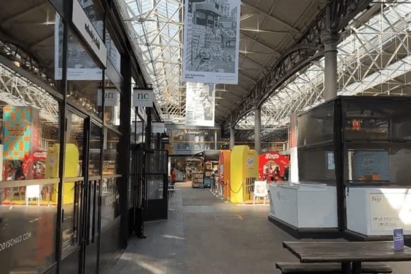 Interior of Old Spitalfields Market with shops, stalls, and a high glass roof structure letting in natural light.