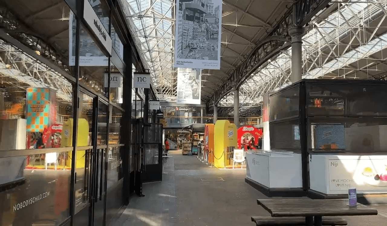 Interior of Old Spitalfields Market with shops, stalls, and a high glass roof structure letting in natural light.