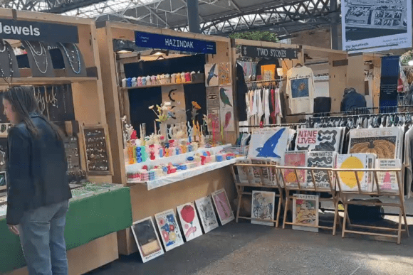 Stalls at Old Spitalfields Market selling jewellery, clothing, artwork, and handmade goods, with shoppers browsing.