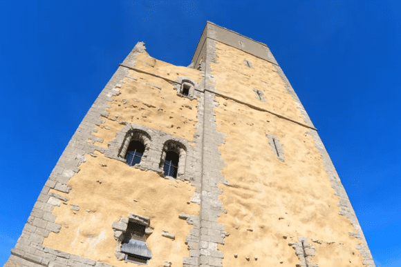 Low-angle view of Orford Castle’s tall stone keep against a clear blue sky.