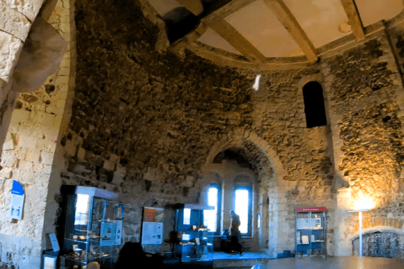 Interior of Orford Castle showing a circular stone room with display cases, arched windows, and exposed wooden beams.